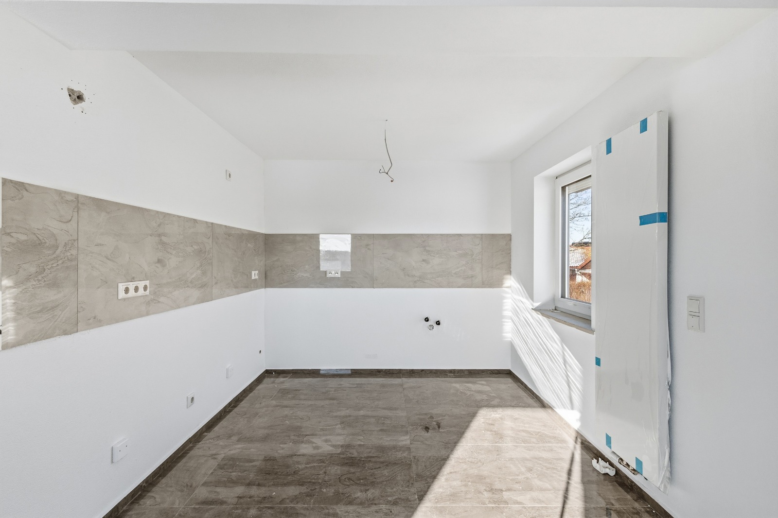 Küche im Rohbau mit Fliesen und offenen Anschlüssen