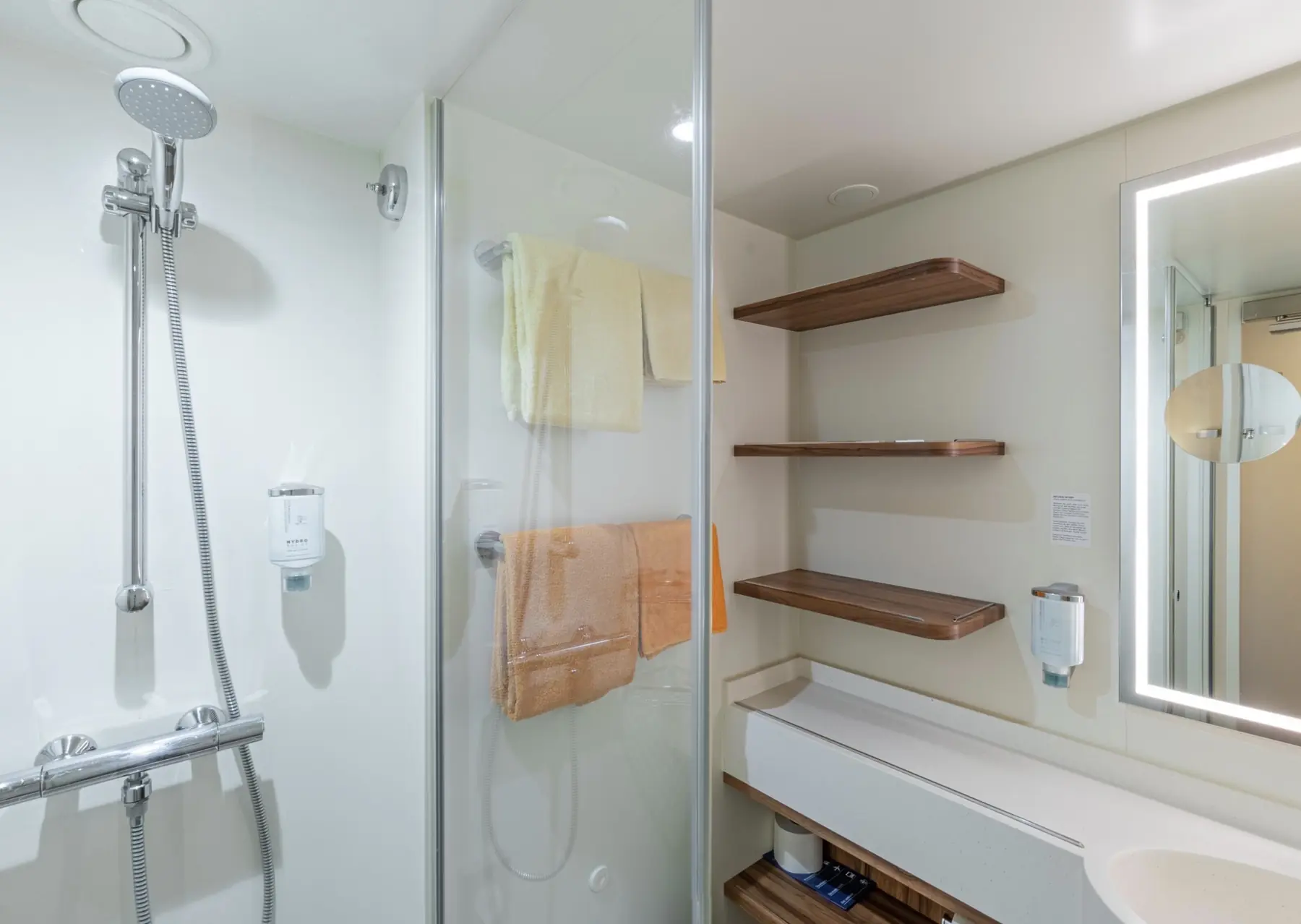 Kabinenbad auf der AIDAperla mit Dusche, beleuchtetem Spiegel und offenen Ablagen