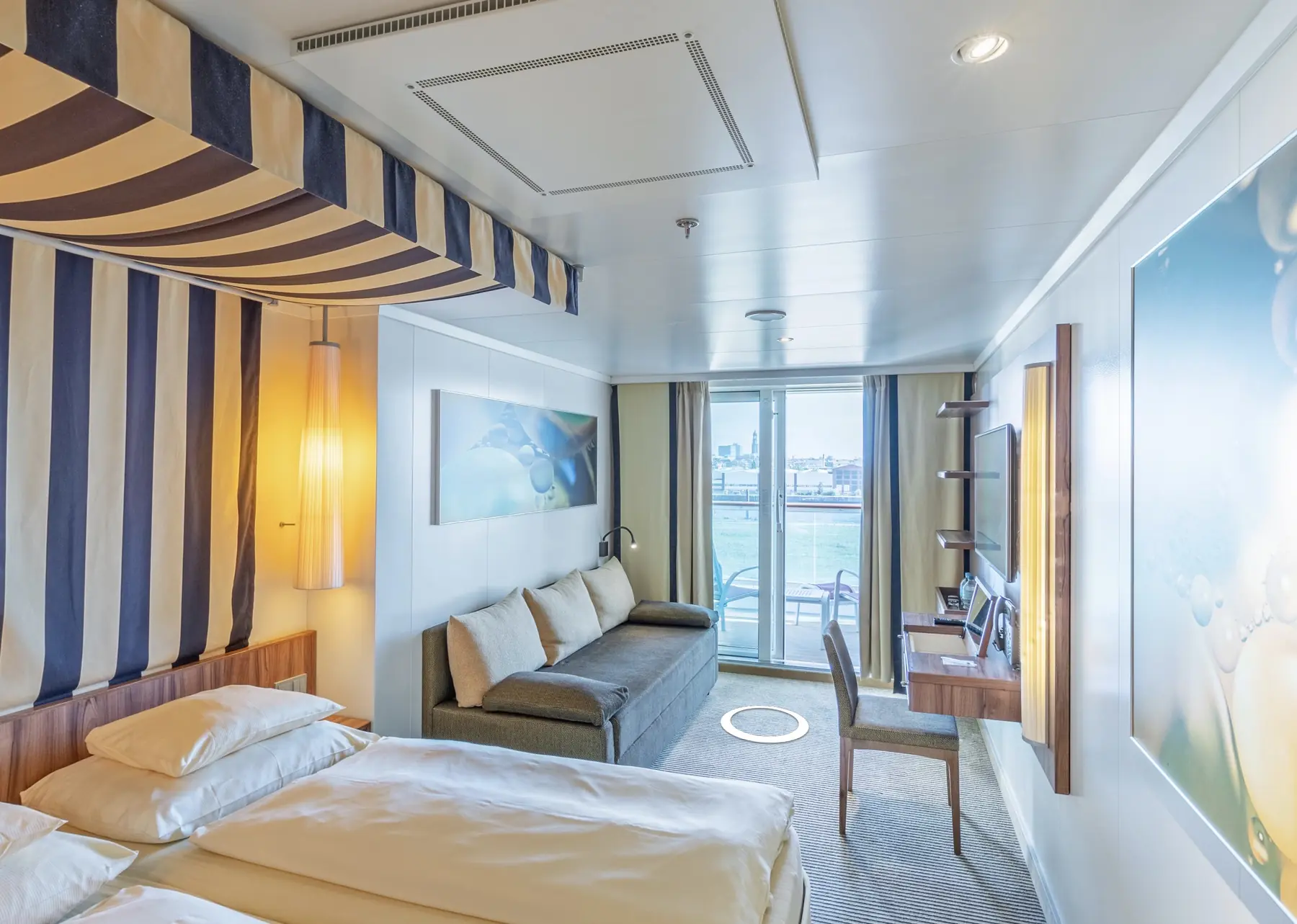 Gästekabine mit Veranda auf der AIDAperla mit Bett, Sofa, Schreibtisch und Blick auf den Außenbereich
