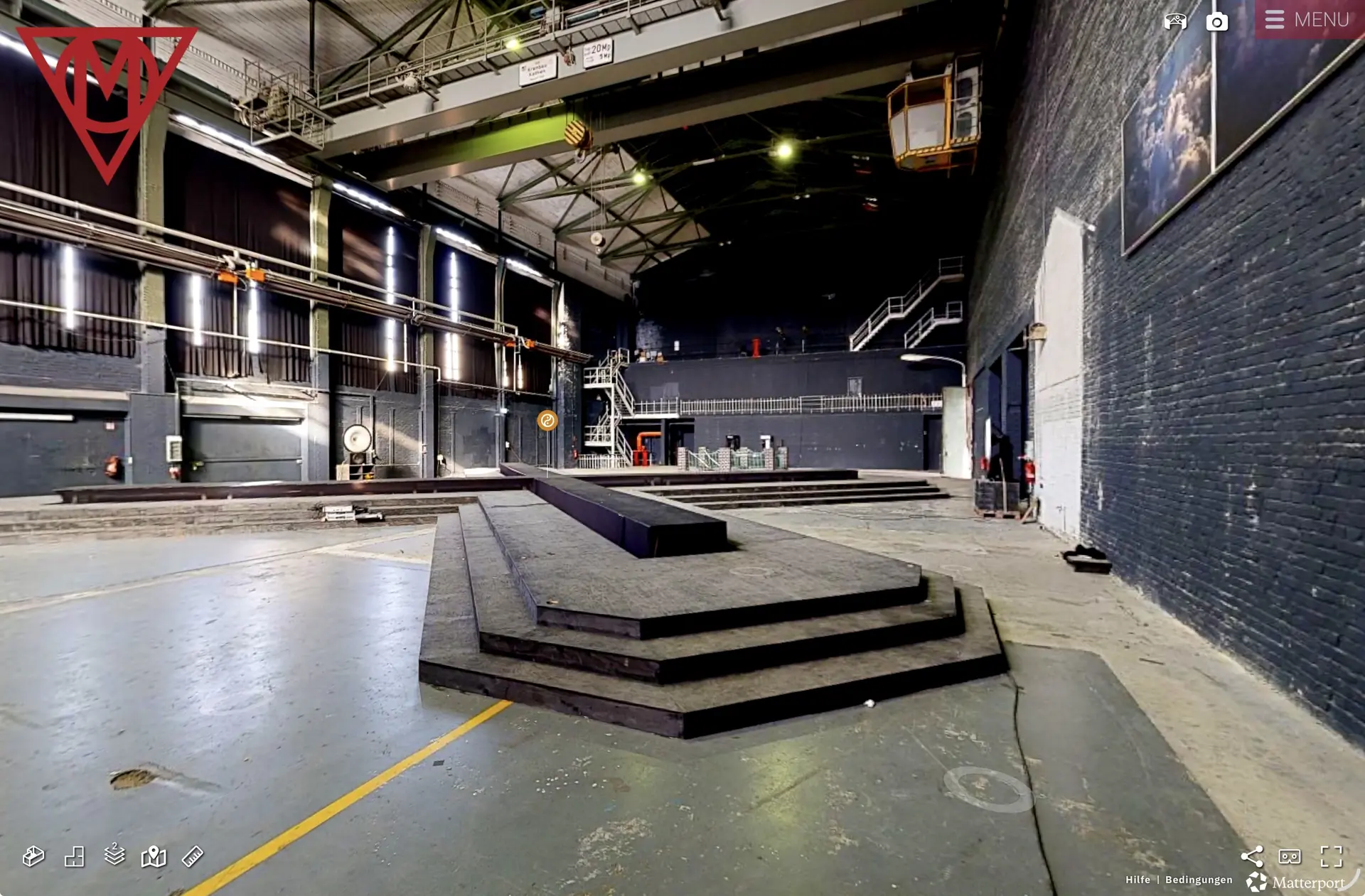 Dunkle Hallenzone der MaHalla mit Bühne, Treppen, Krananlage und schwarz gefassten Backsteinwänden