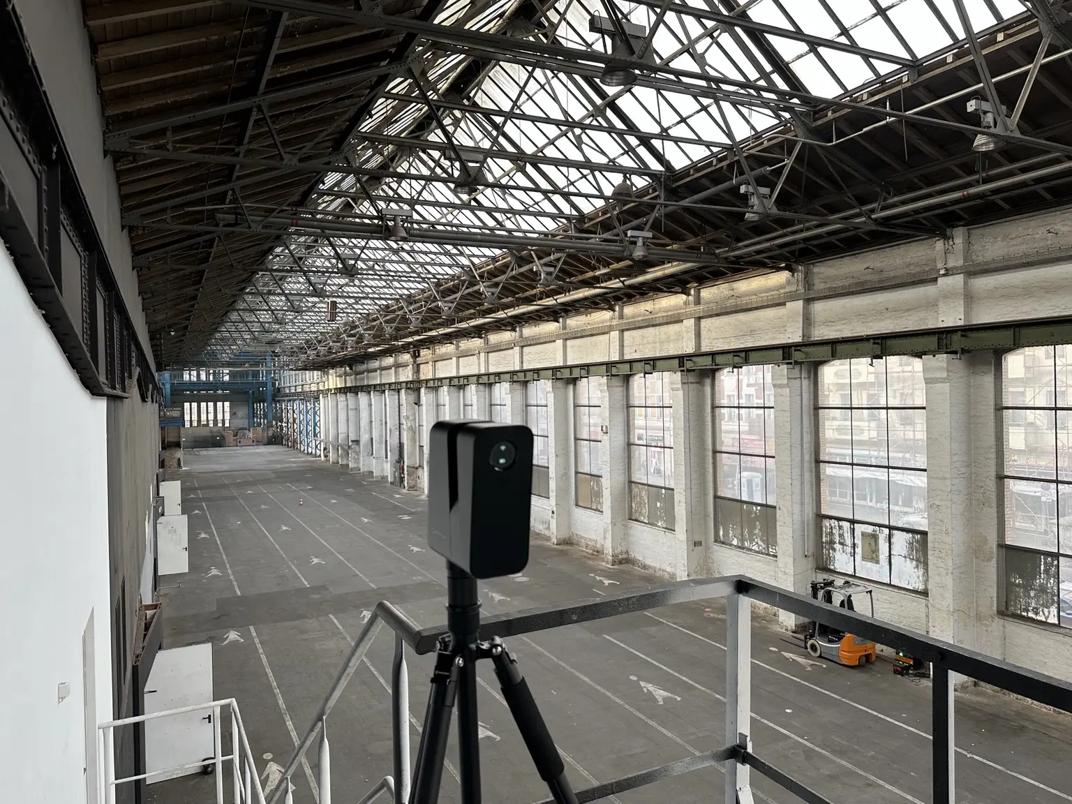 3D-Scanner auf einer Empore mit Blick entlang einer großen Industriehalle und ihres Stahlfachwerkdachs.