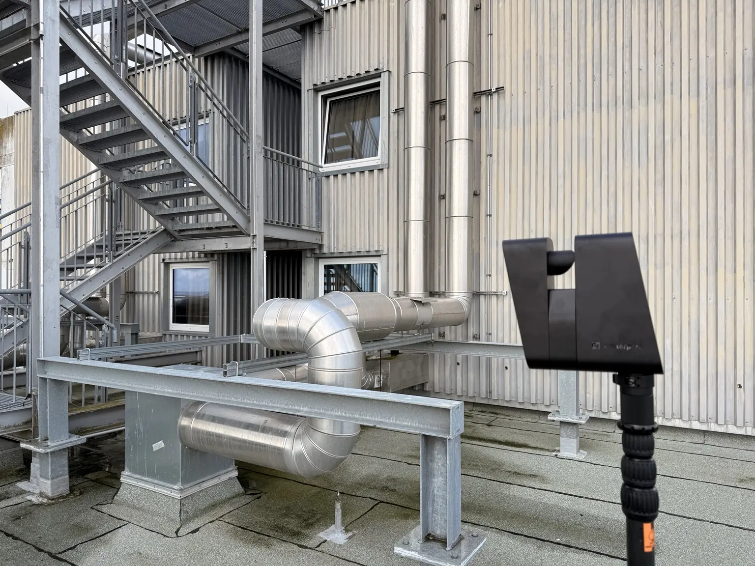 Matterport Pro3 auf einem Dachpodest vor Metallfassade, Außentreppe und Gebäudetechnik