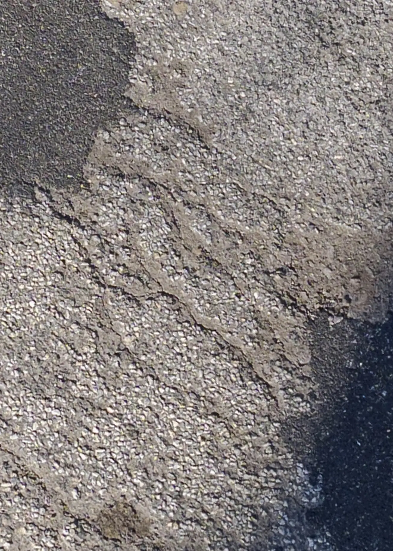 Stark vergrößerter Webausschnitt einer Asphaltoberfläche mit feiner Rissstruktur an einer Materialgrenze.